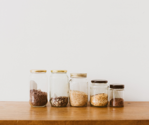 Jars half filled with food lined up by size on a wooden surface with a white background.